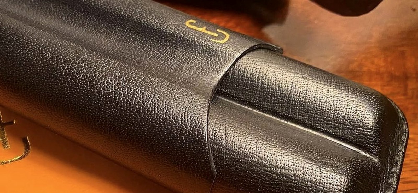 A handmade leather cigar case beside a cigar and enamel ashtray
