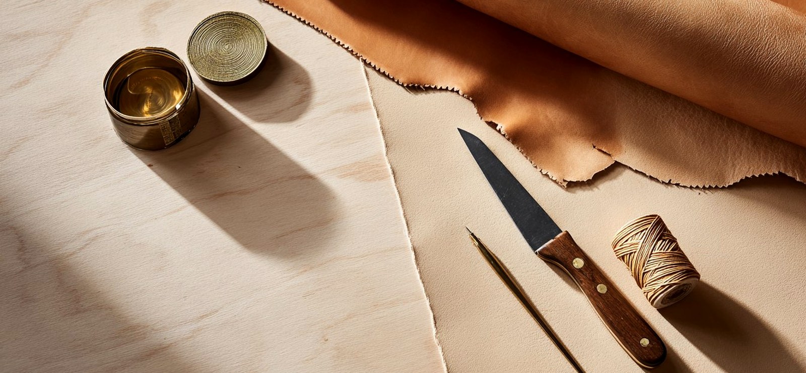 Leatherworking tools — knife, awl, waxed thread and a full-grain hide on the bench